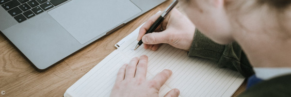 Mensch, der auf ein Blatt Papier schreibt